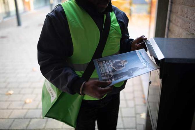 promo koerier steekt een gemeentelijke infoblad in een brievenbus